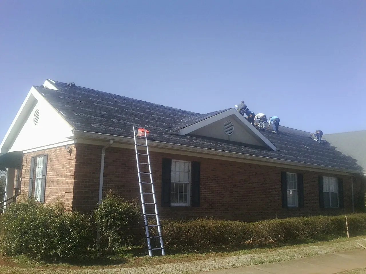 Crew tearing shingles off a brick ranch roof with a ladder set — Metal Roof Repair work by our crew in Frederick